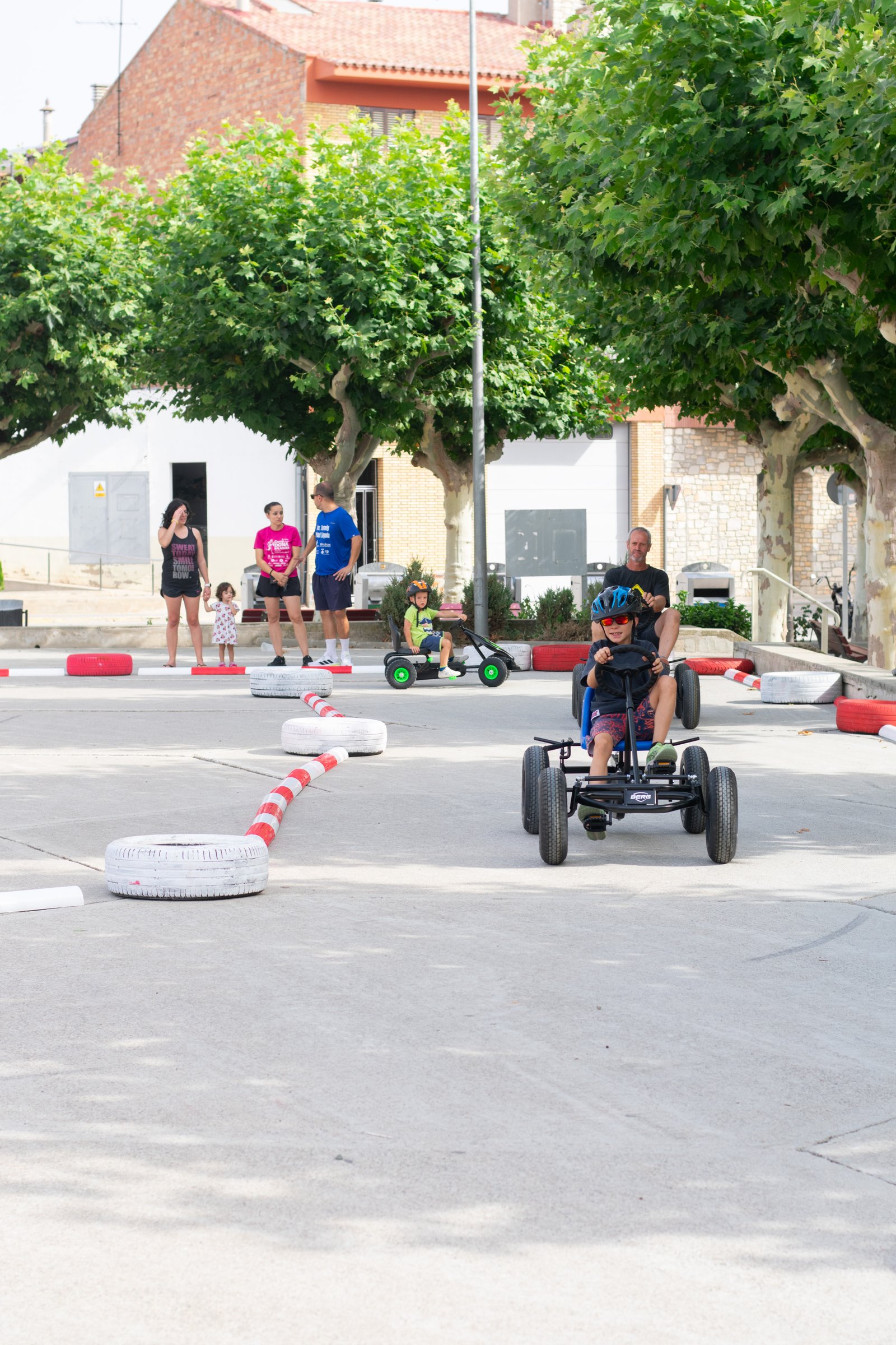 Grupo de niños y adultos conduciendo karts a pedales en un circuito urbano